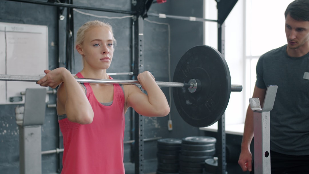Gym athlete using fitness tracking app on phone between sets at squat rack