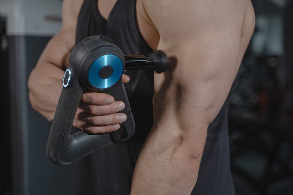 Theragun Prime percussion massage gun on a gym floor next to trainers and a water bottle