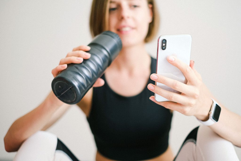 a woman looking at her fitness app on her phone while drinking fluids